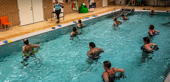 Ungt par utövar vattenträning med instruktör i motionsbassäng.